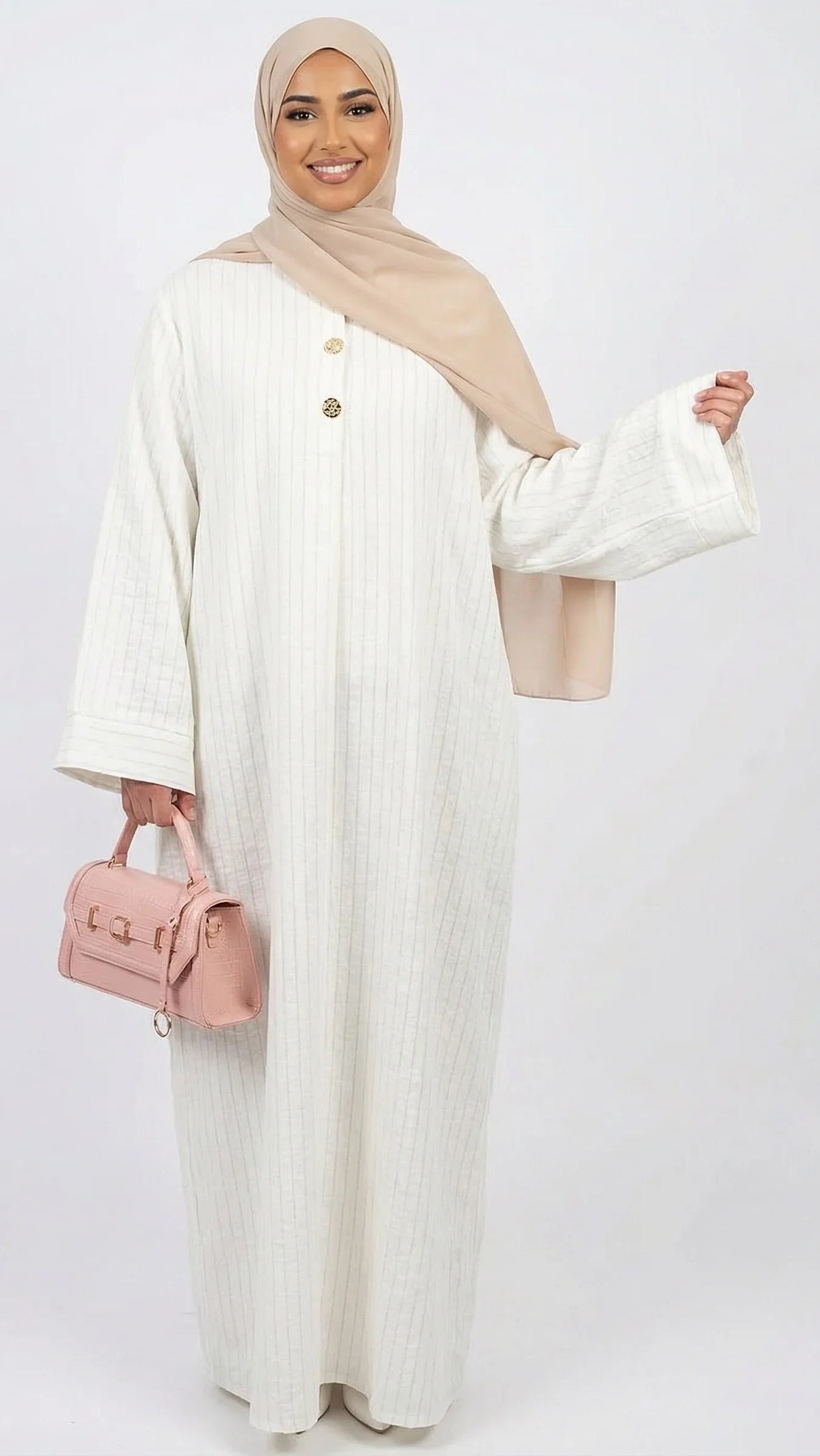 Femme portant une abaya blanche, un hijab beige et un sac à main rose, mode modeste Muneera.