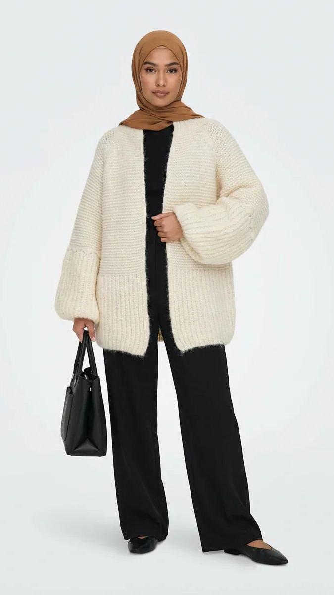 Femme en cardigan oversize crème Muneera, pantalon noir, hijab marron, sac noir, style mode modeste.