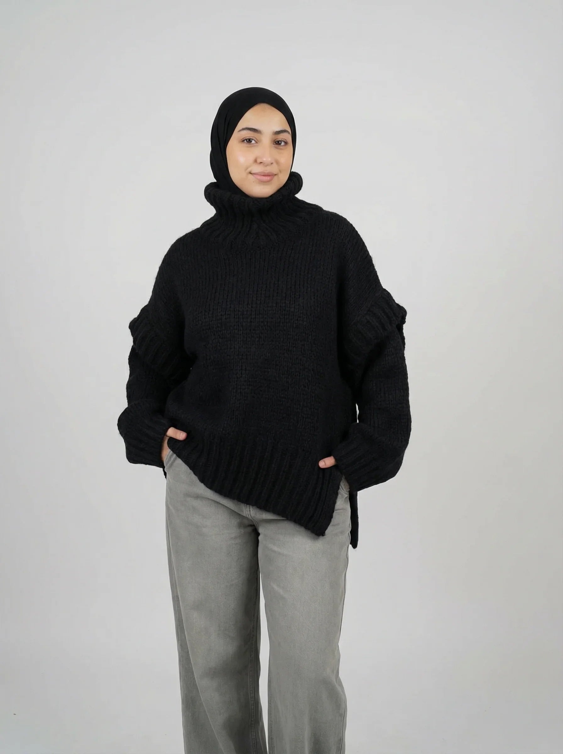 Femme en pull noir en maille Muneera, style mode modeste, pantalon gris, hijab noir