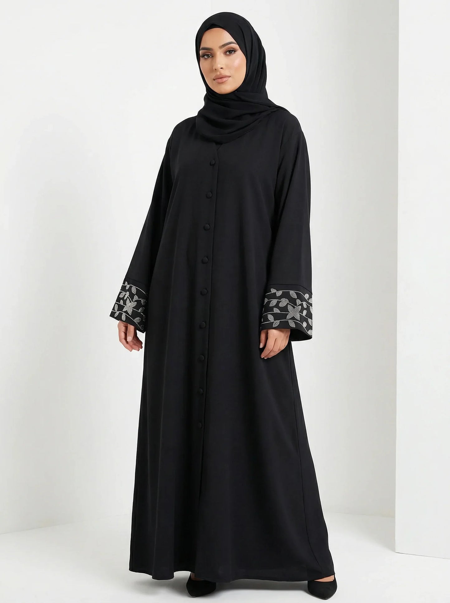 Femme musulmane en abaya noire élégante Muneera, manches brodées, mode modeste moderne.