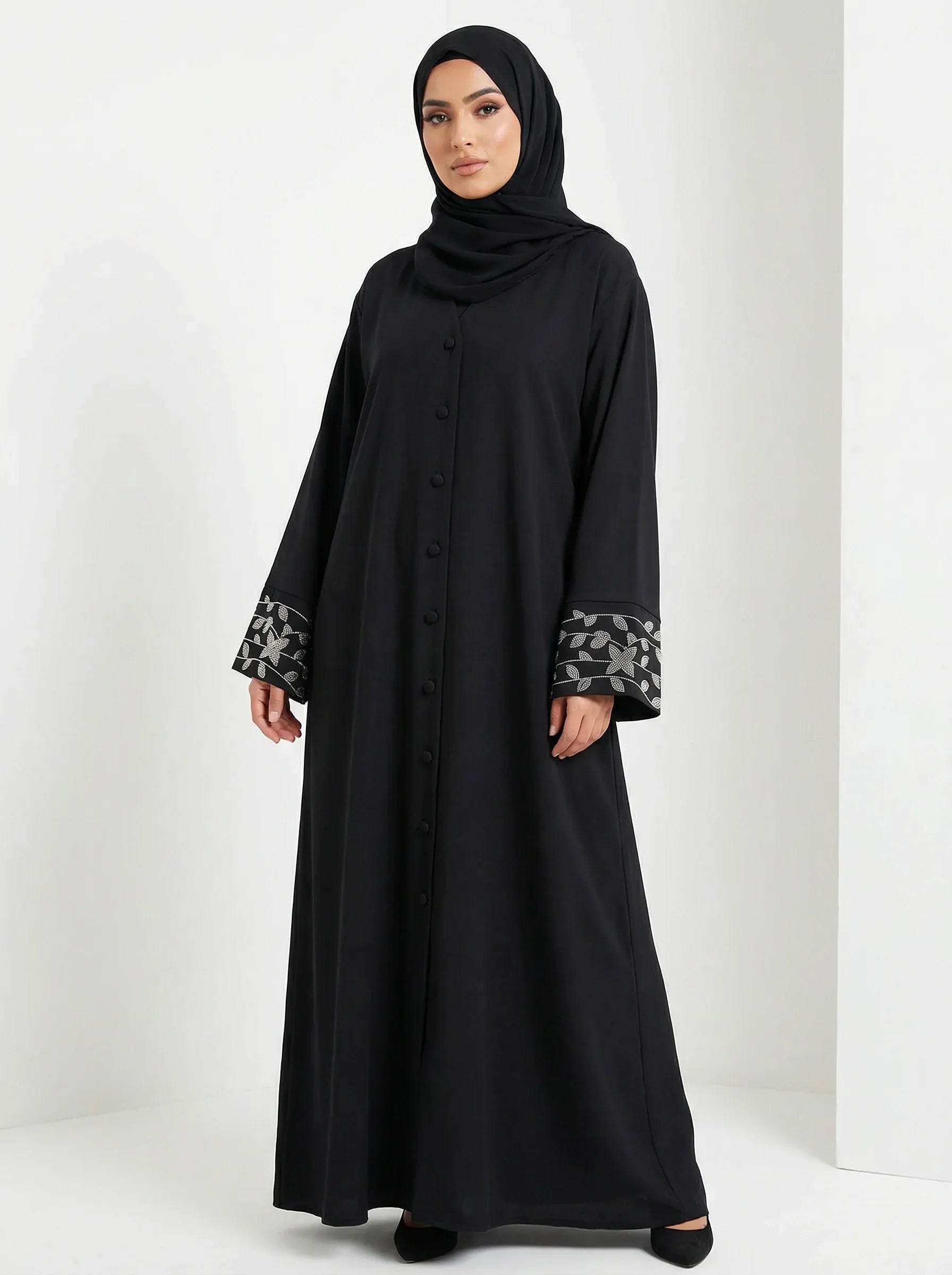 Femme musulmane en abaya noire élégante Muneera, manches brodées, mode modeste moderne.