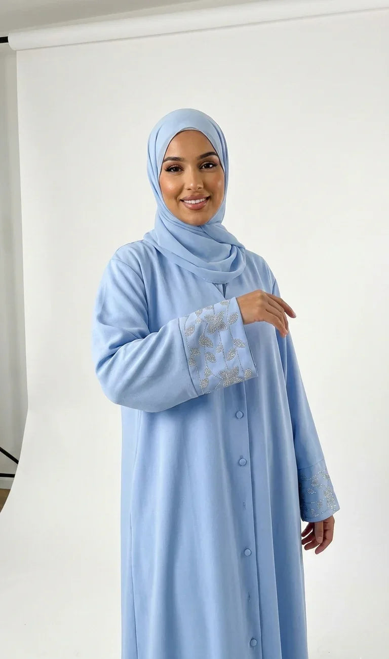 Femme souriante en abaya bleu clair à manches brodées, mode modeste Muneera.