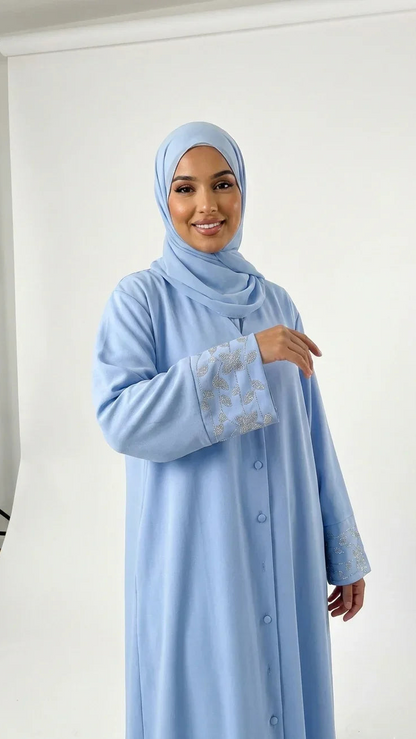 Femme souriante en abaya bleu clair à manches brodées, mode modeste Muneera.