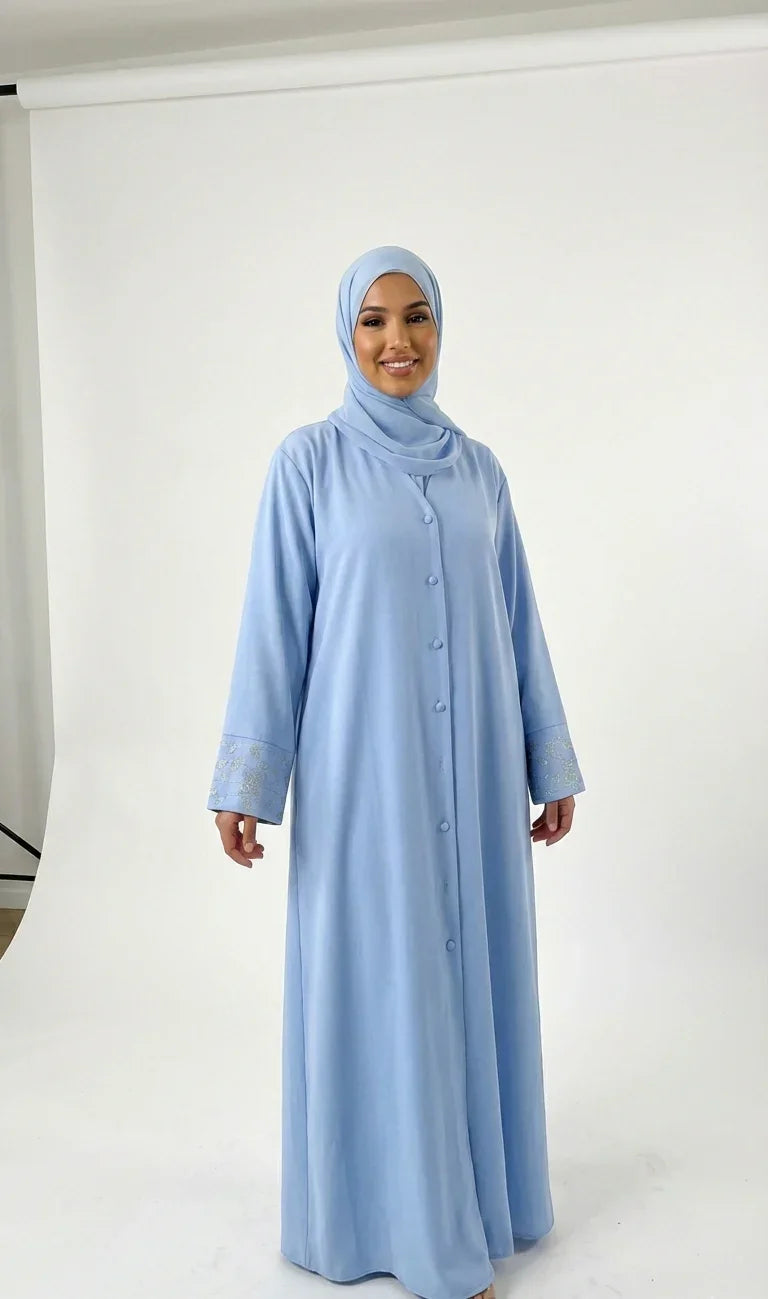 Femme portant une abaya bleue élégante Muneera, mode modeste moderne sur fond studio blanc.