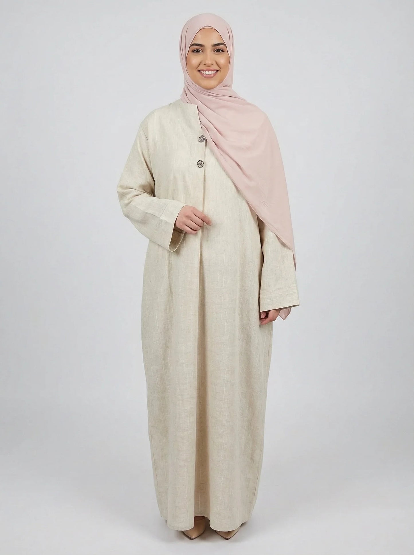 Femme souriante portant une abaya beige élégante Muneera et un hijab rose, mode modeste moderne.