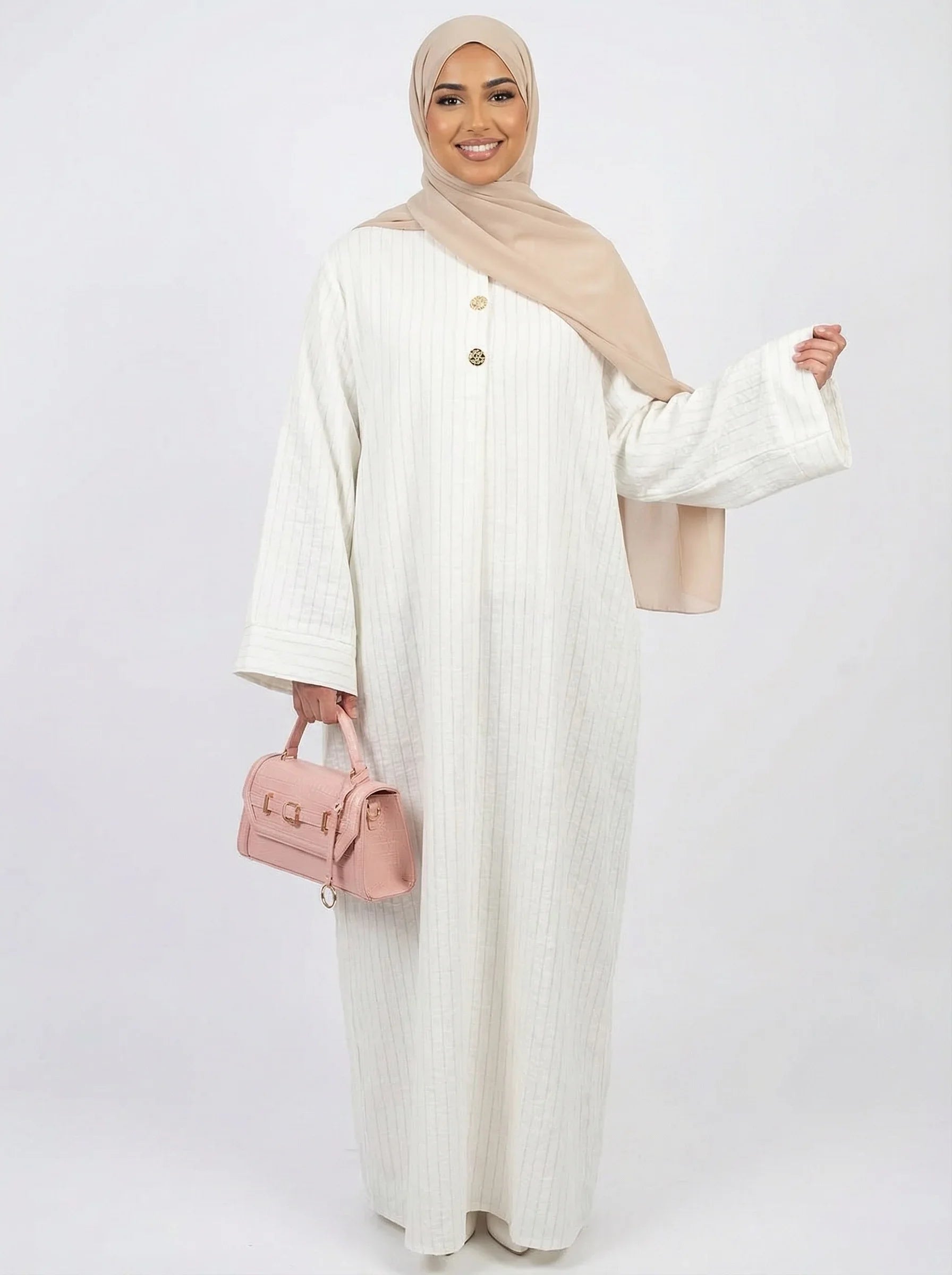 Femme portant une abaya blanche, un hijab beige et un sac à main rose, mode modeste Muneera.