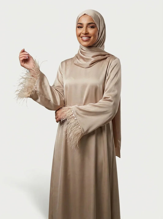 Femme souriante en abaya beige satinée Muneera, manches plumes, mode modeste élégante.