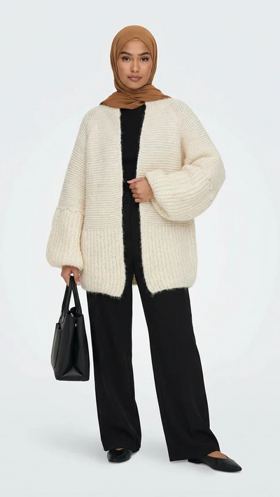 Femme en cardigan oversize crème Muneera, pantalon noir, hijab marron, sac noir, style mode modeste.