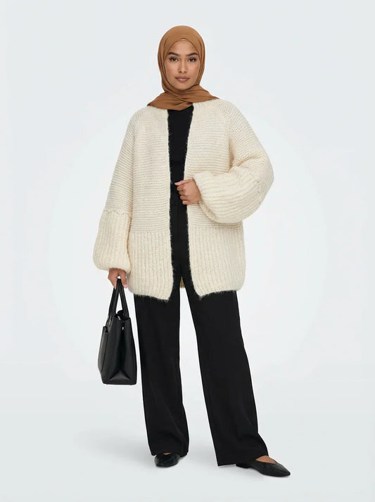 Femme en cardigan oversize crème Muneera, pantalon noir, hijab marron, sac noir, style mode modeste.