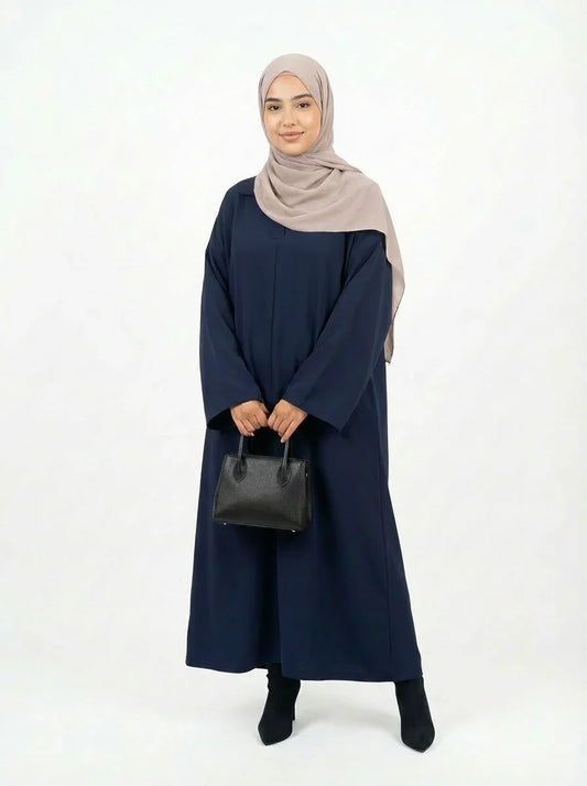 Femme portant une robe bleue longue et un hijab beige, sac noir, mode modeste Muneera.